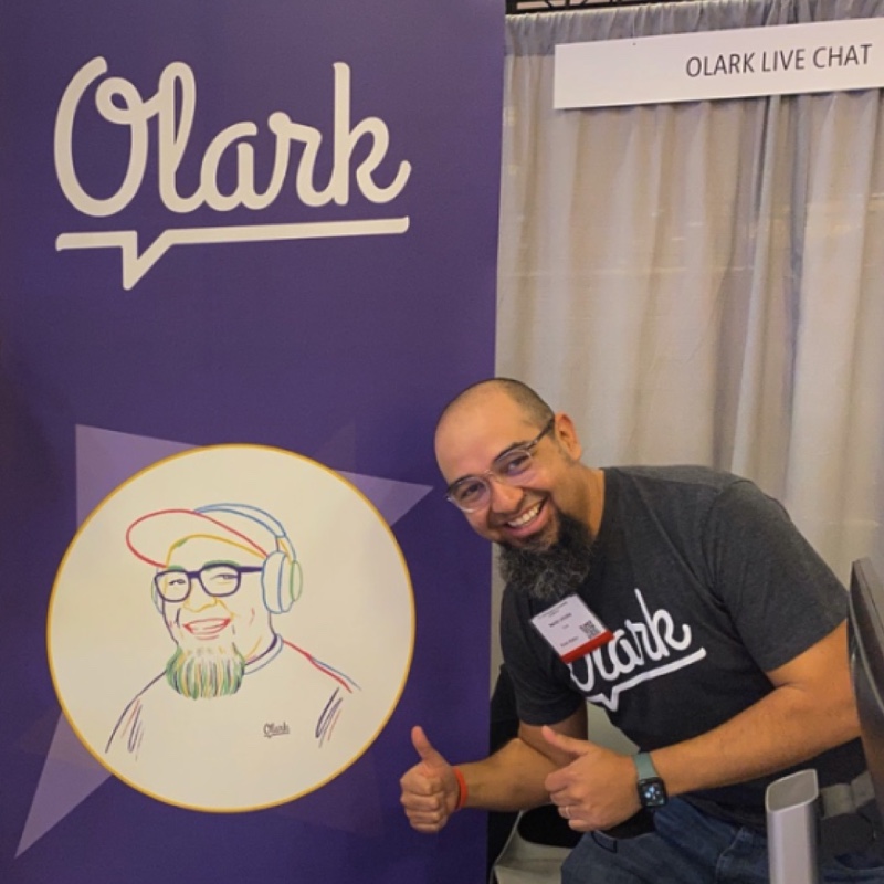 An Olarker giving a thumbs up in front of Olark's CSUN booth.