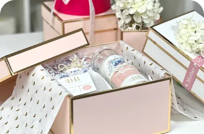 A pink gift box with gold trim filled with tissue paper and gift items